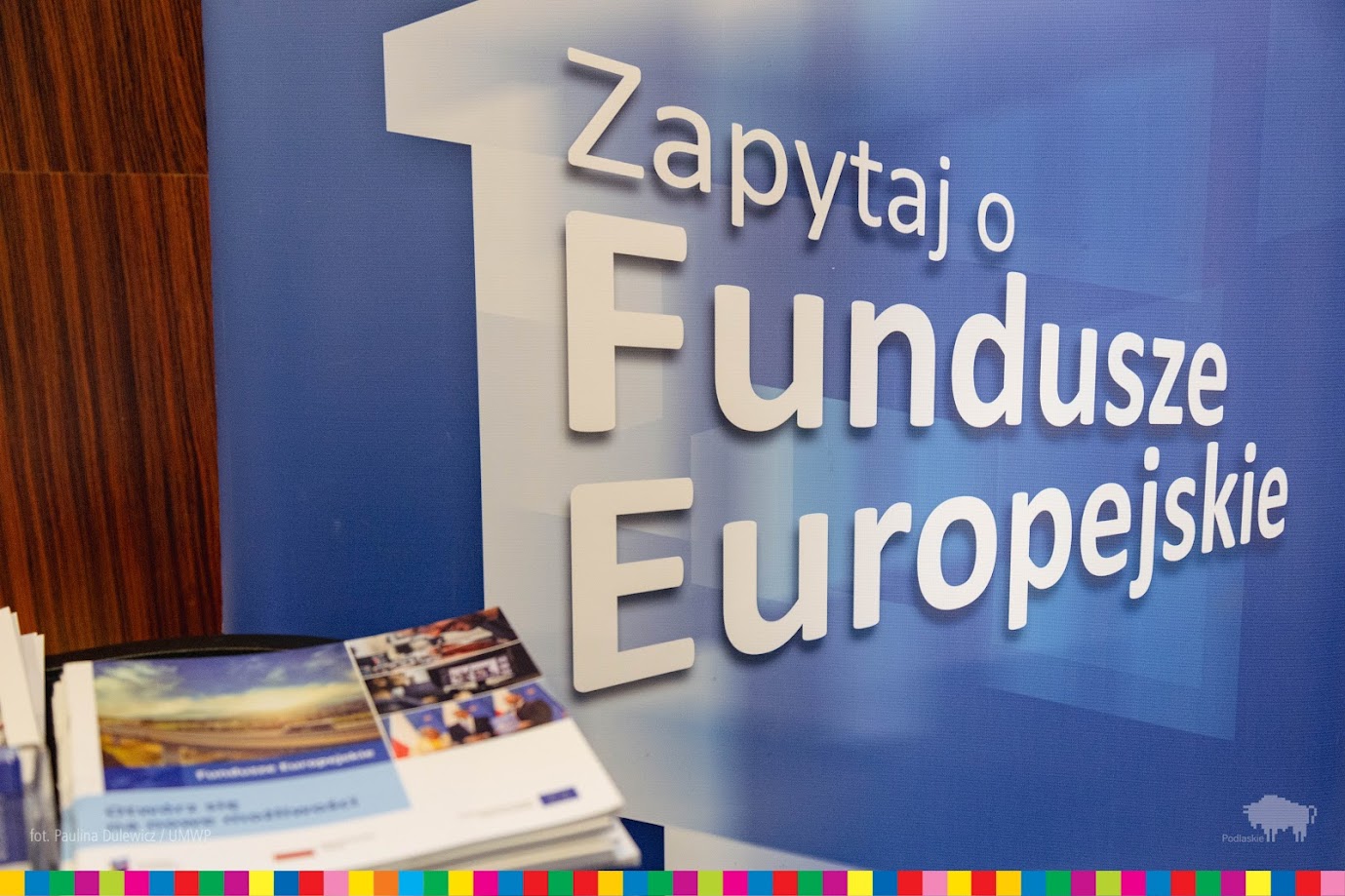 Stolik z ulotkami i baner z napisem "Zapytaj o Fundusze Europejskie"