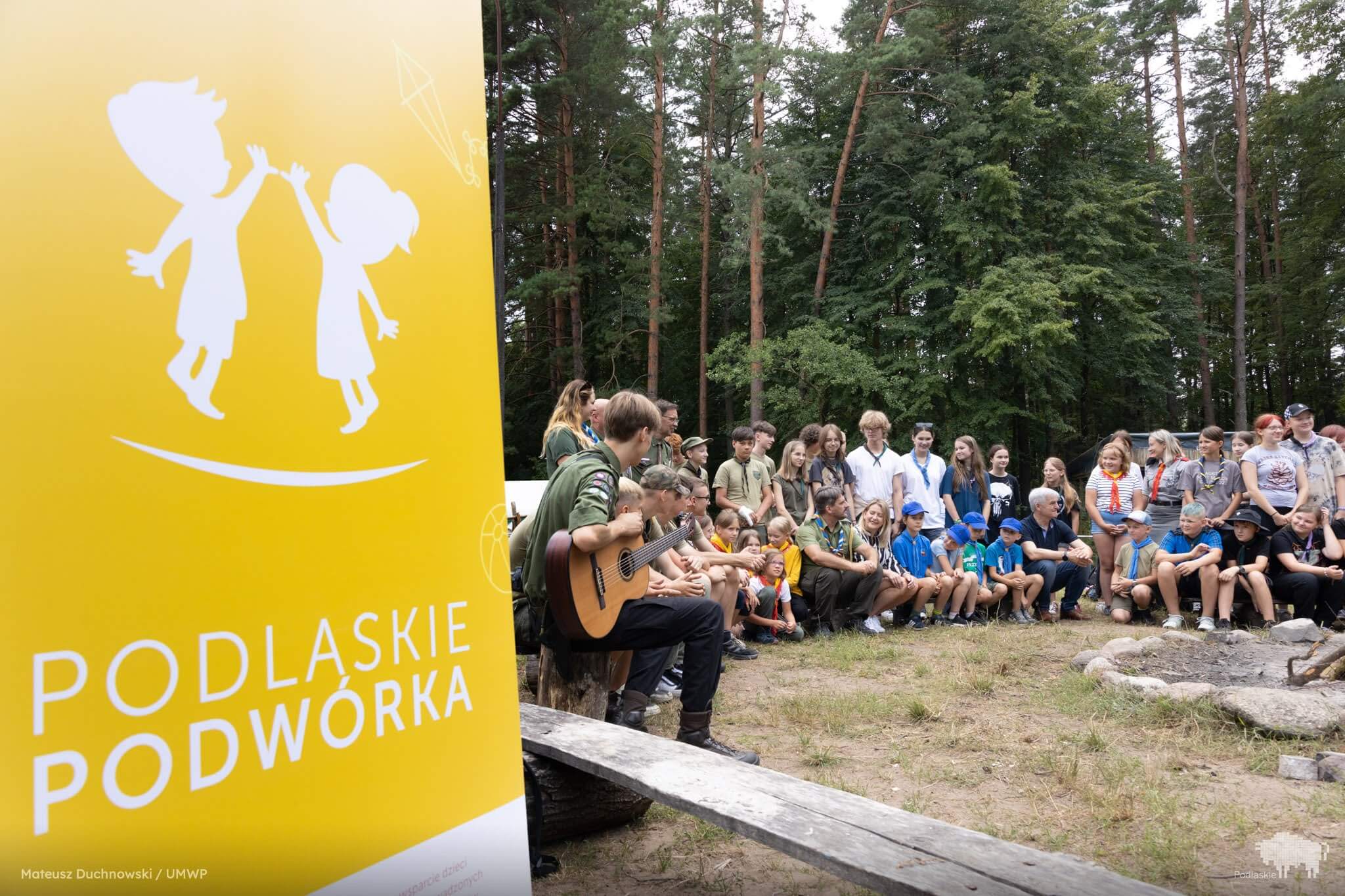 Obozowicze siedzą w kręgu wokół miejsca na ognisko