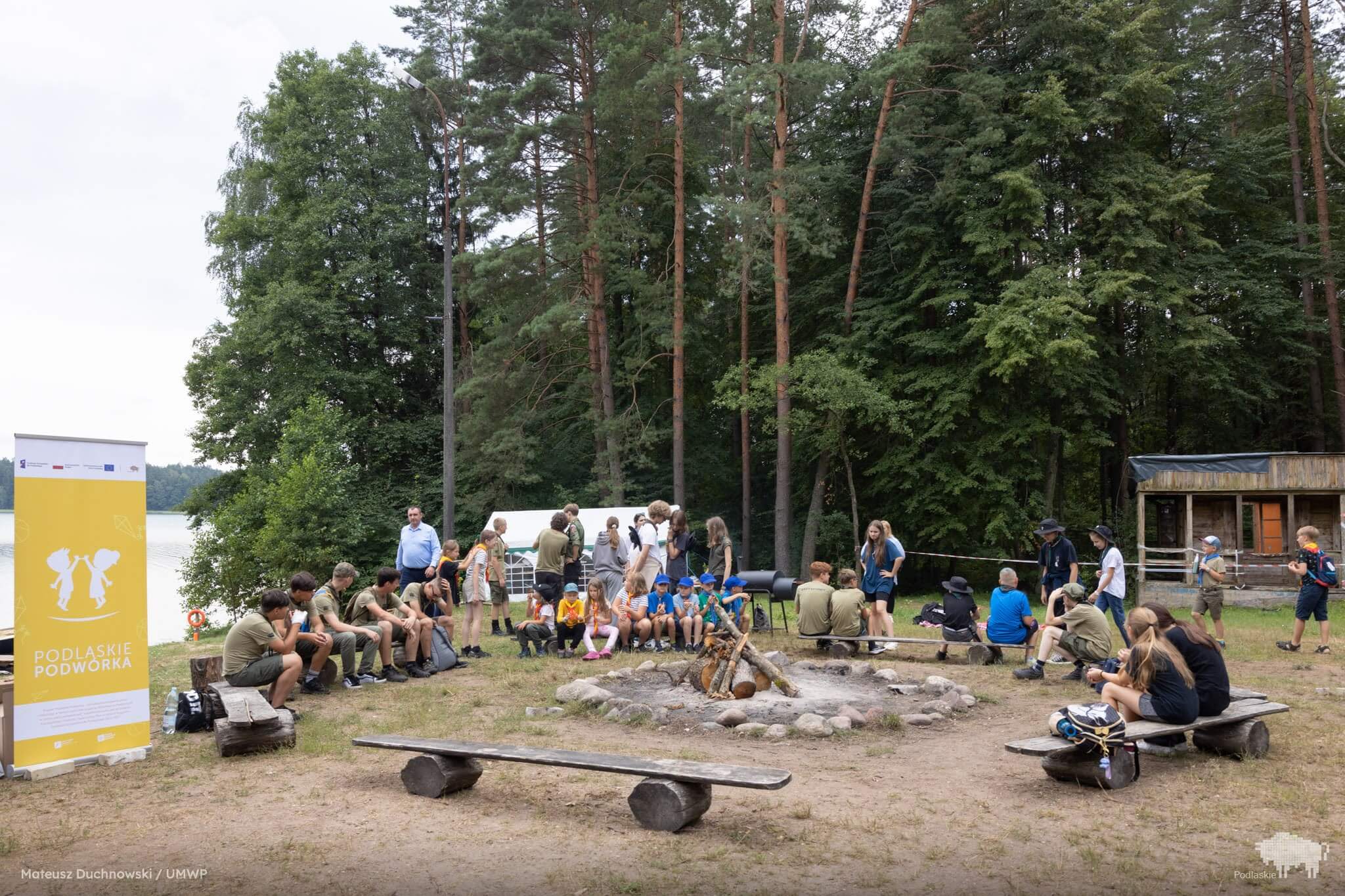 Obozowicze siedzą w kręgu wokół miejsca na ognisko