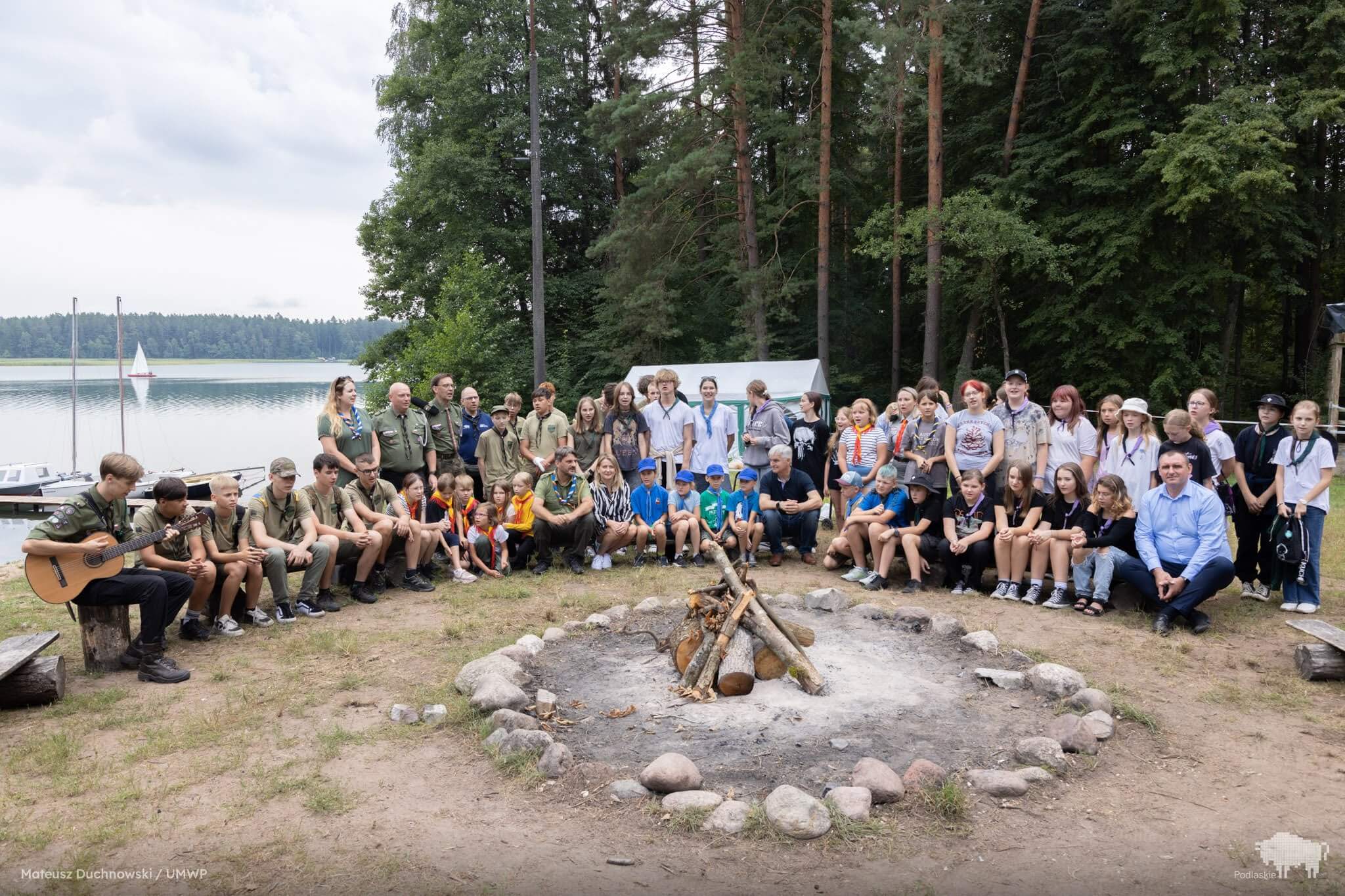 Obozowicze siedzą w kręgu wokół miejsca na ognisko