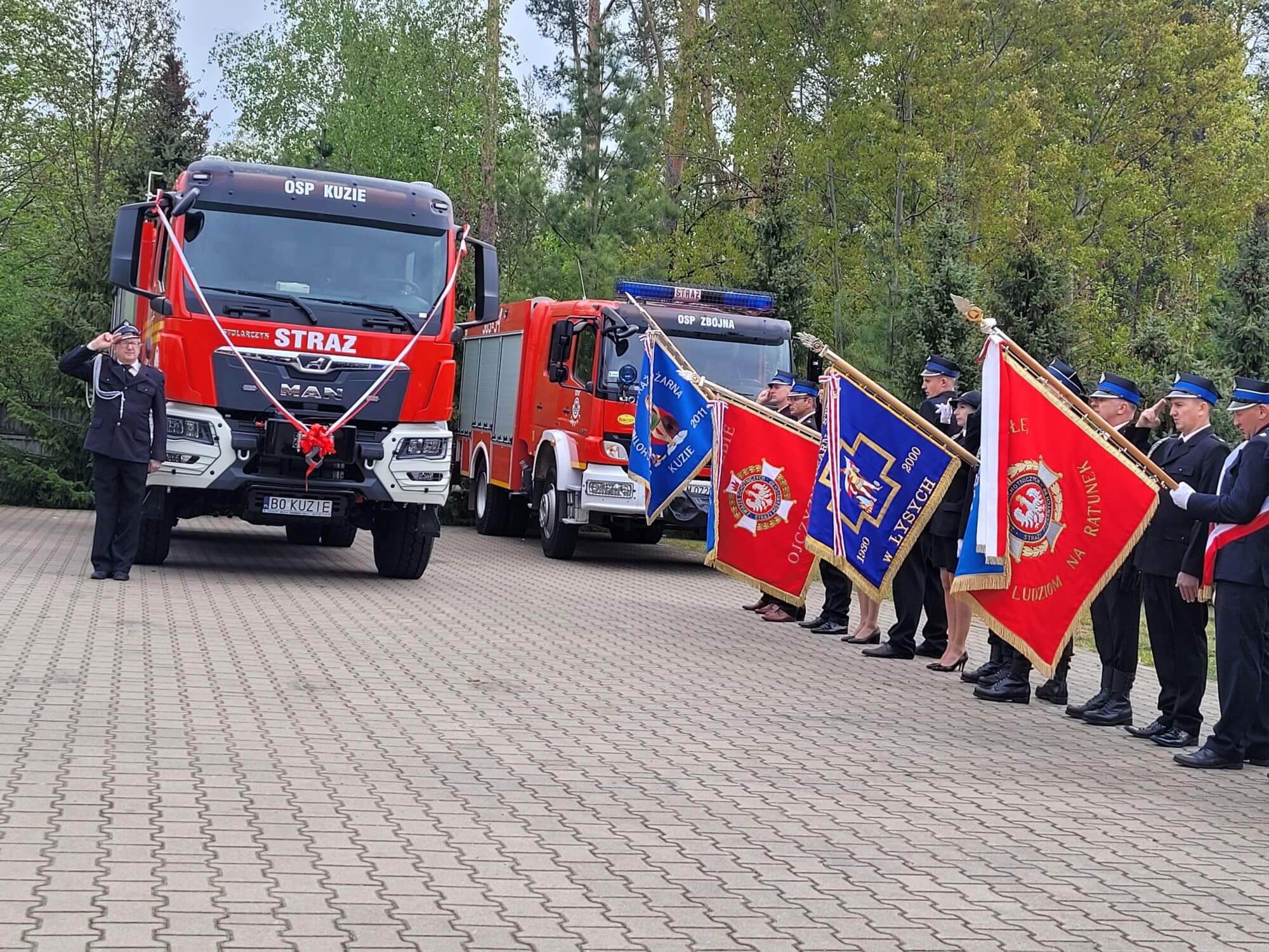 Poczet sztandarowy OSP. W tle wozy strażackie