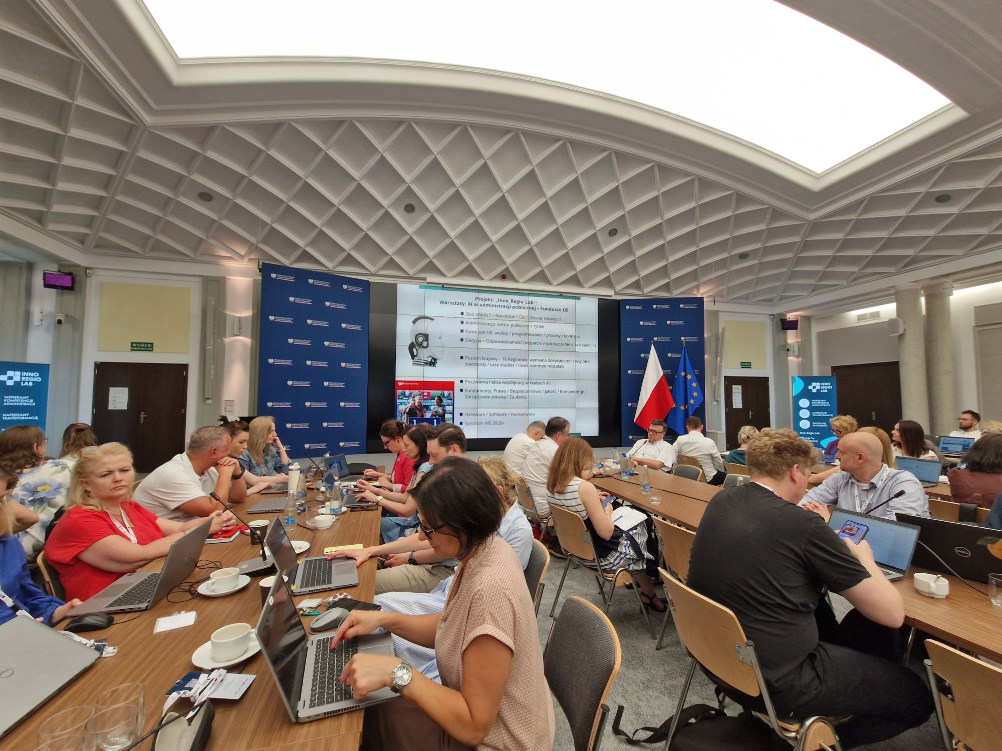 Grupa osób siedzi przy stołach w czasie szkolenia