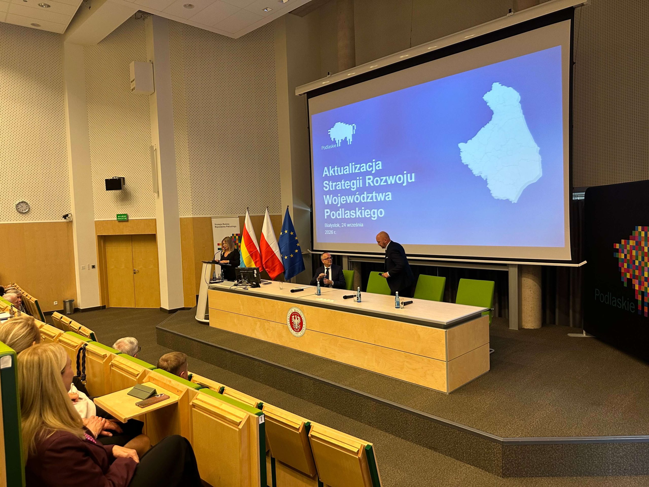 Uczestnicy spotkania siedzą przy stole prezydialnym