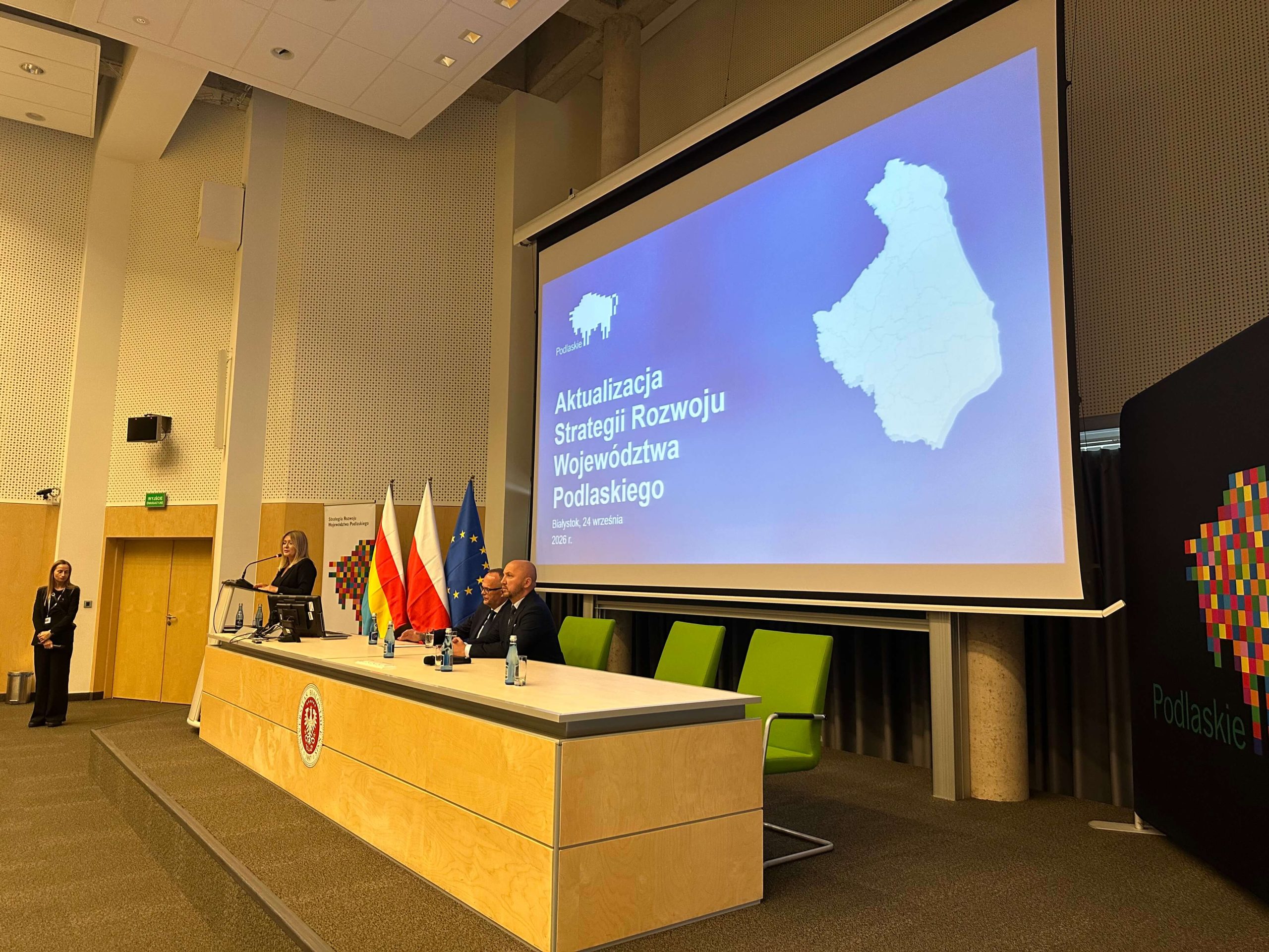 Uczestnicy spotkania siedzą przy stole prezydialnym