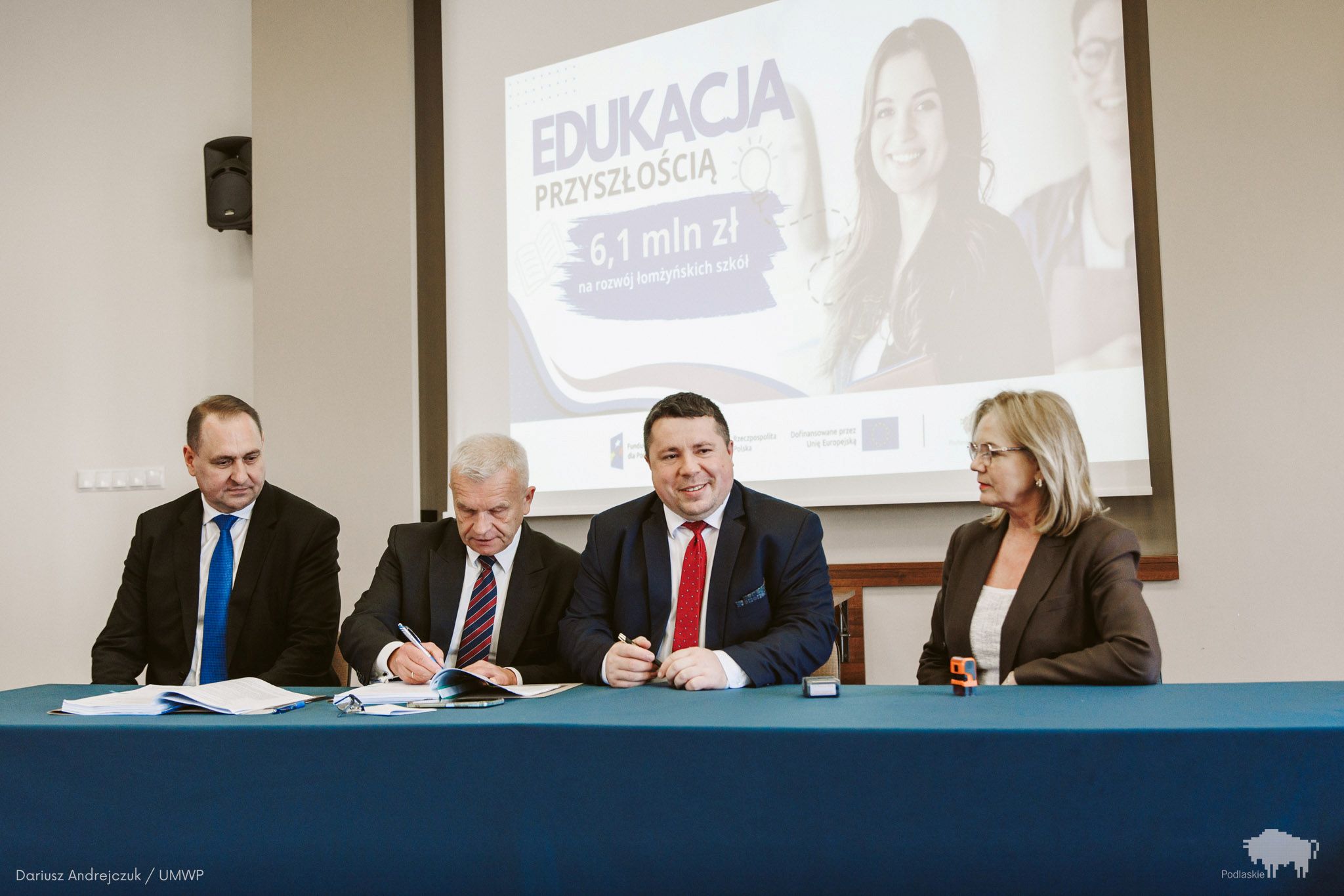 Grupa osób podpisuje dokument.